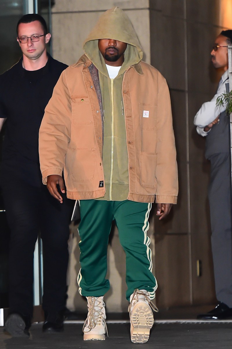 Kanye West Walking down the street wearing green Adidas tracksuit bottoms, matched with a green hoodie and a beige jacket